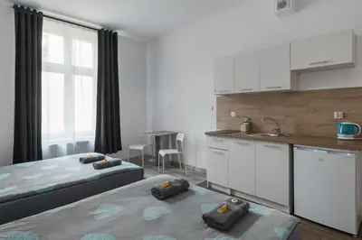 a white bedroom with a bed and a kitchen at 70s Business Room in Kraków