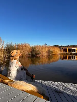 a woman sitting on a dock next to a body of water at Raj na Hektarach in Wysokie