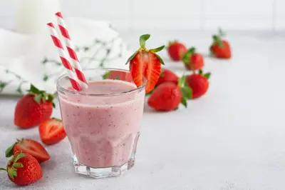 a glass of strawberry smoothie with strawberries in the background at Cheerful Air Conditioned Apartment with mezzanine and Parking - Old Town in Kraków